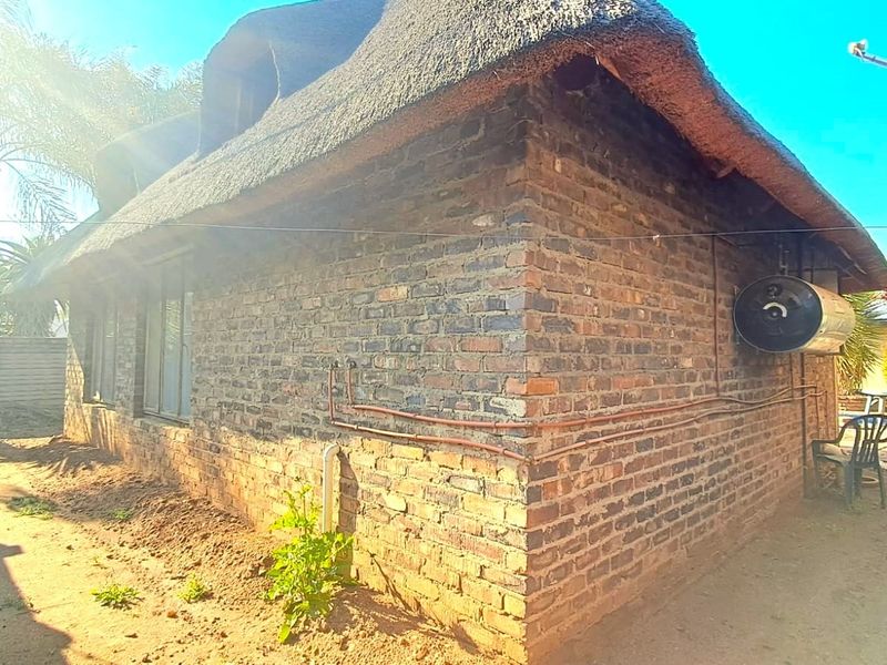 Rear view of a flat featuring a traditional thatch roof, exposed brick exterior walls, and an external geyser unit.