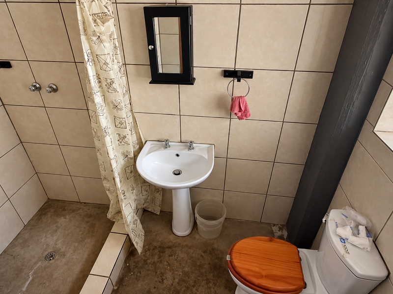 A functional bathroom featuring a pedestal basin, shower area, and toilet with tiled wall finishes and a concrete floor.