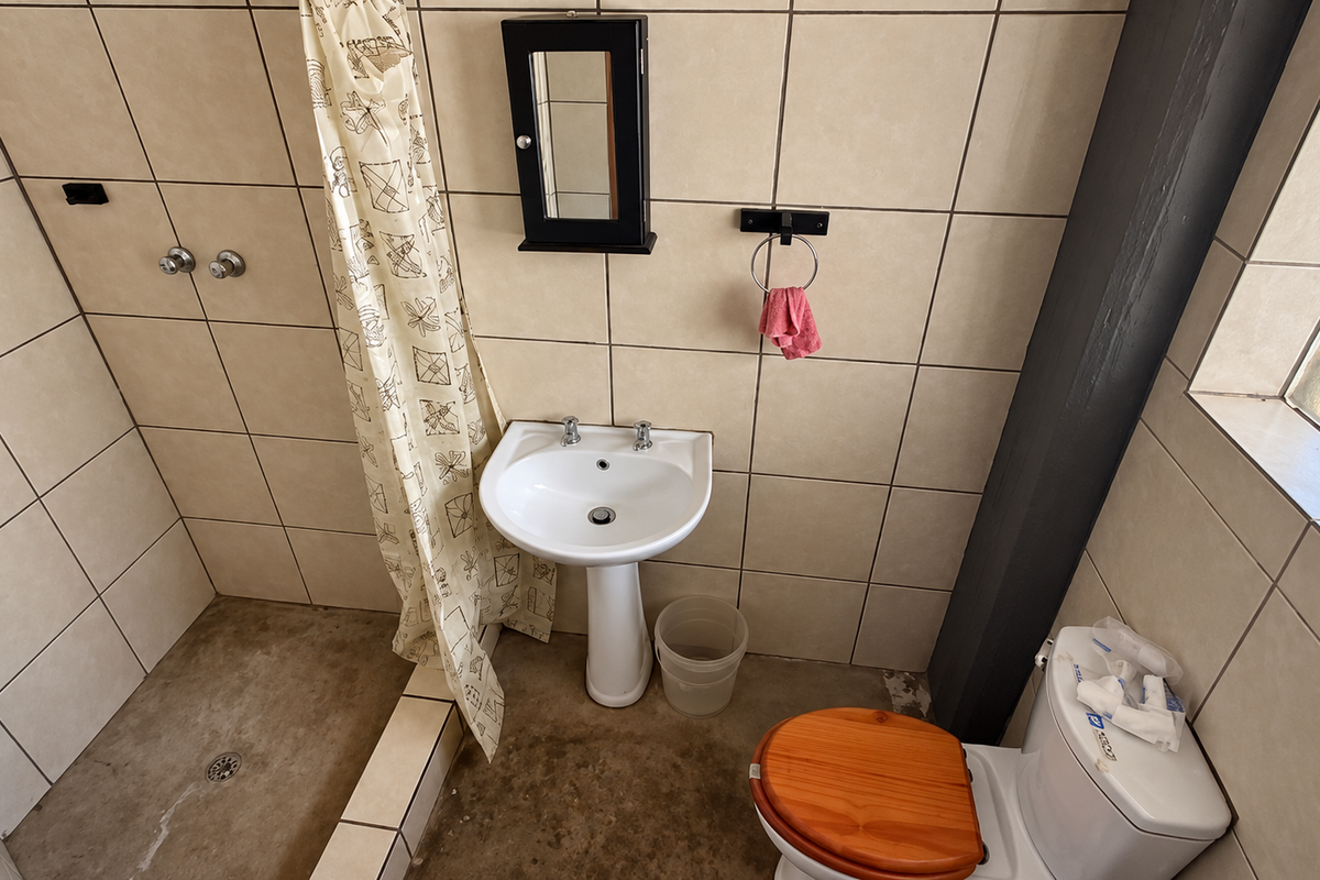 A functional bathroom featuring a pedestal basin, shower area, and toilet with tiled wall finishes and a concrete floor.