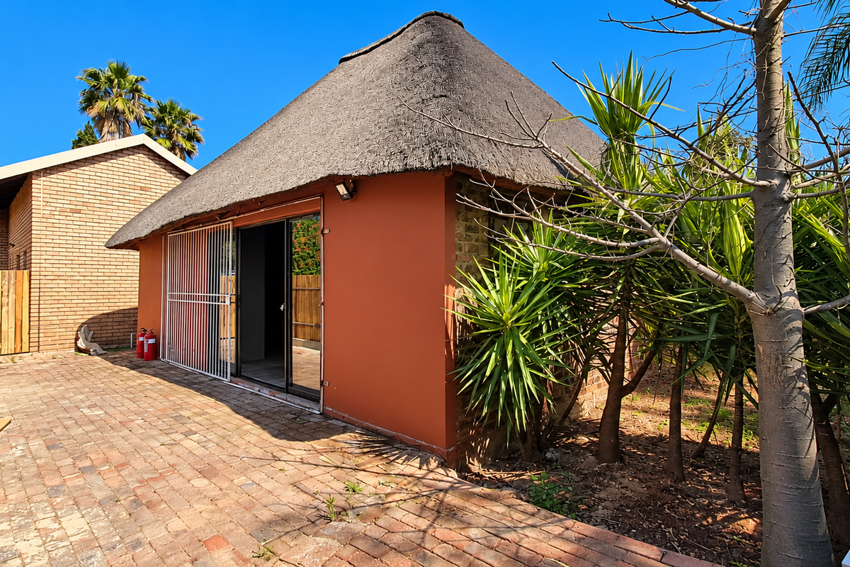 Rear view of a property featuring a thatch-roofed structure with a sliding glass door, security gate, and brick-paved patio area.
