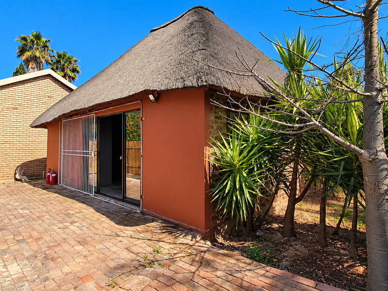 Rear view of a property featuring a thatch-roofed structure with a sliding glass door, security gate, and brick-paved patio area.