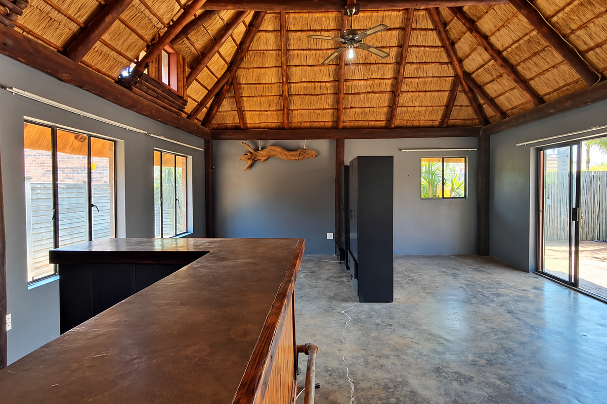 Spacious bar area featuring a high thatched roof with exposed timber beams, concrete flooring, and a built-in bar counter, opening onto an outdoor patio.