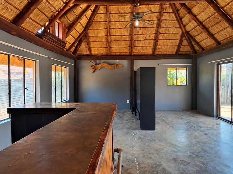 Spacious bar area featuring a high thatched roof with exposed timber beams, concrete flooring, and a built-in bar counter, opening onto an outdoor patio.