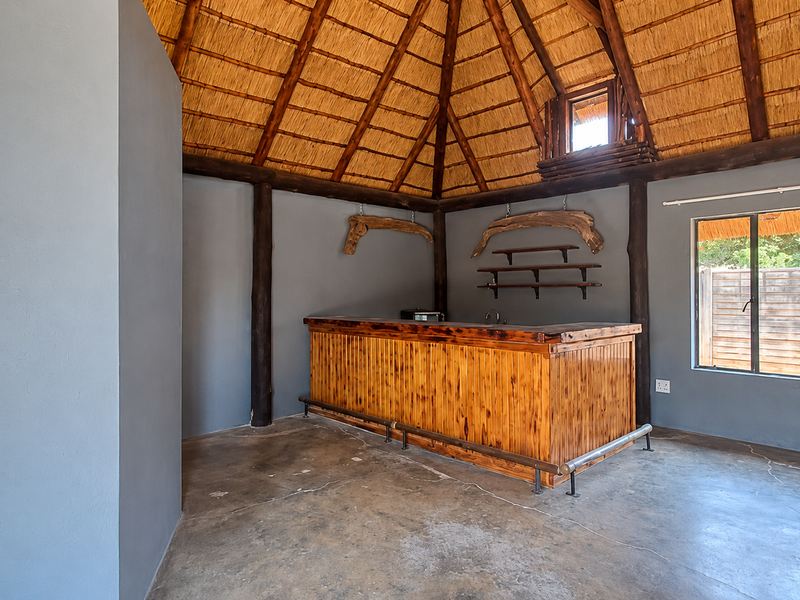 A rustic bar area featuring a high thatched ceiling with exposed timber beams, a built-in wooden bar counter, and polished concrete flooring.