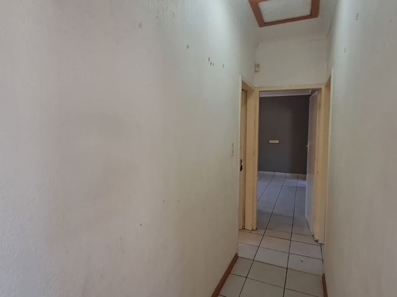 A vacant interior hallway featuring tiled flooring and access to adjacent rooms, requiring cosmetic updates to the wall finishes.