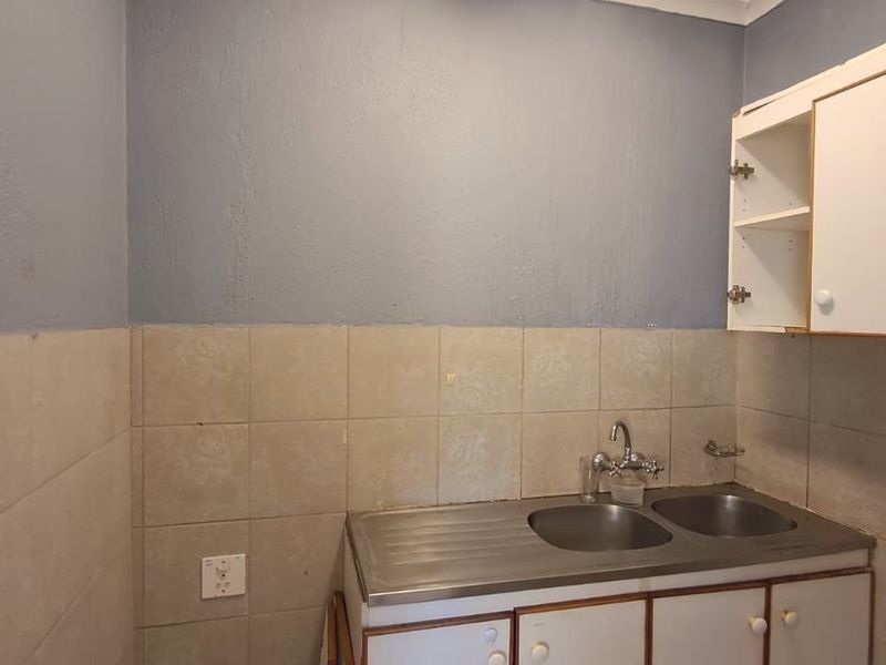 A compact kitchen area featuring a stainless steel double sink, tiled splashback, and built-in cabinetry requiring some maintenance and cosmetic updates.