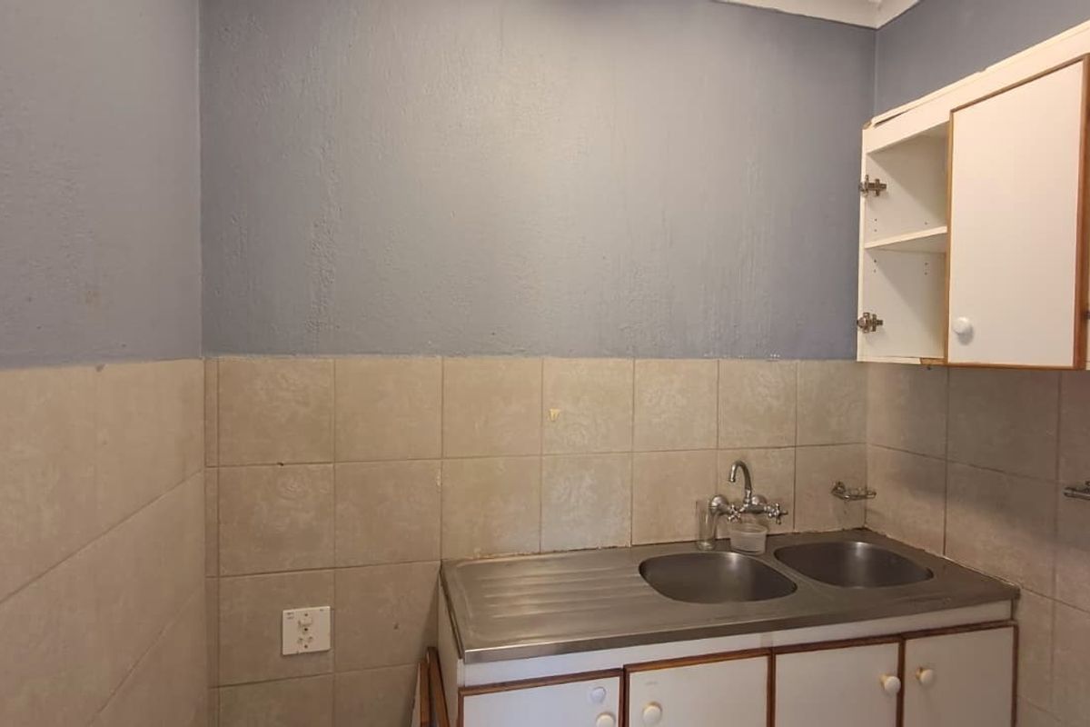 A compact kitchen area featuring a stainless steel double sink, tiled splashback, and built-in cabinetry requiring some maintenance and cosmetic updates.