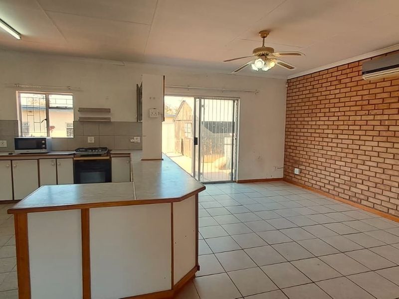 Spacious open-plan living and kitchen area featuring tiled floors, an exposed brick wall, built-in cabinetry, and direct access to the exterior via a sliding door.