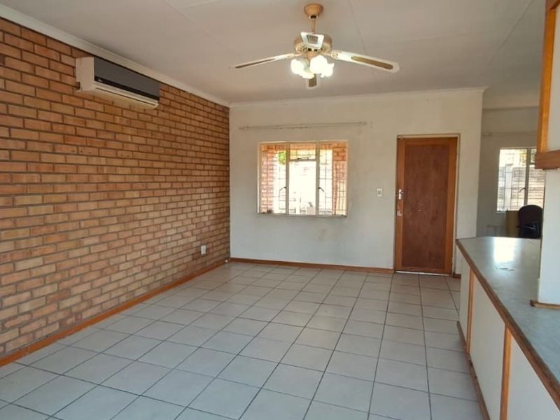 Open-plan living area featuring tiled floors, an exposed brick feature wall, ceiling fan, and split-system air conditioning, with an adjacent kitchen counter.