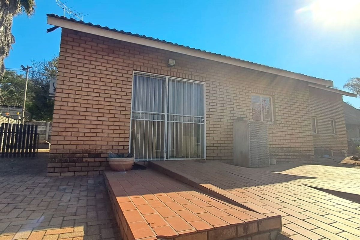 Rear exterior view of the flat featuring a face brick facade, paved patio area with a ramp, and secure metal gate access.