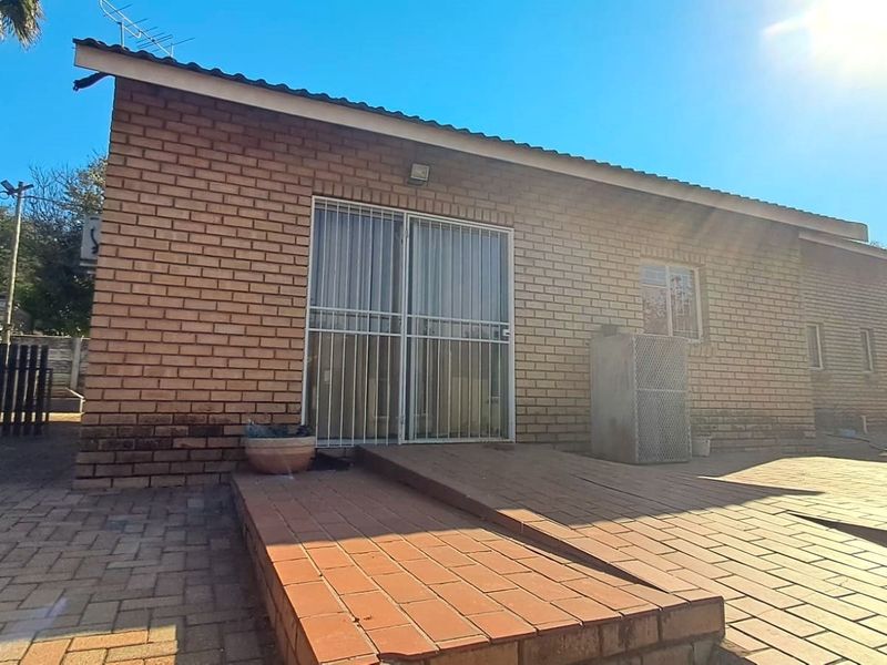 Rear exterior view of the flat featuring a face brick facade, paved patio area with a ramp, and secure metal gate access.