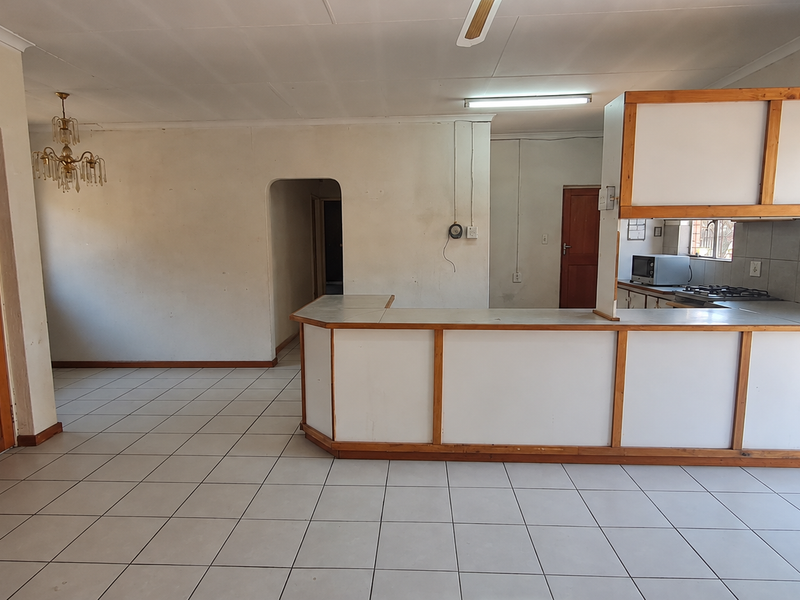 Open-plan living and kitchen area featuring tiled flooring, a breakfast bar, and built-in cabinetry, offering a blank canvas for renovation.