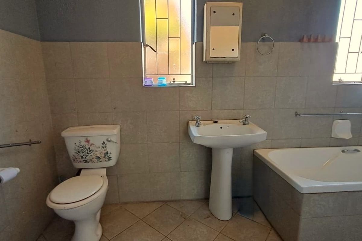 A functional bathroom featuring a pedestal basin, built-in bathtub, and toilet, finished with neutral wall and floor tiles.