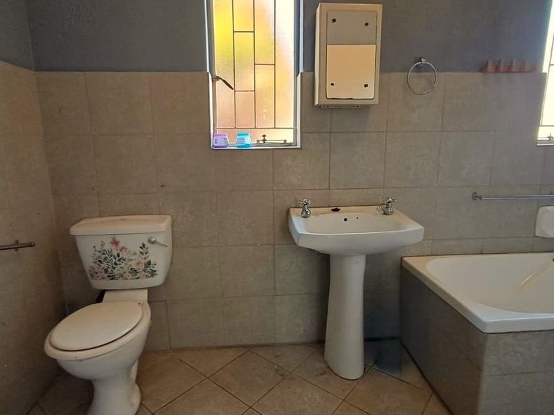 A functional bathroom featuring a pedestal basin, built-in bathtub, and toilet, finished with neutral wall and floor tiles.