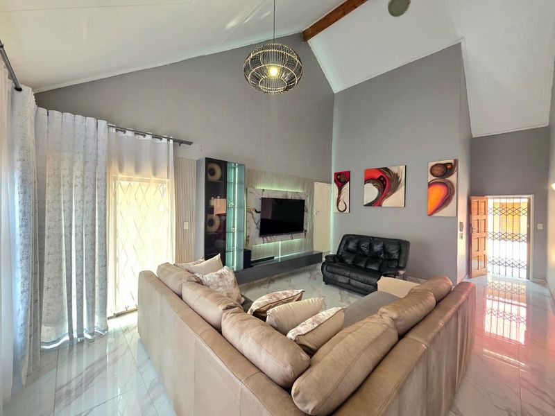 Spacious living room featuring a high vaulted ceiling with exposed timber beam, marble-look tiled flooring, and a modern built-in media wall with integrated lighting.