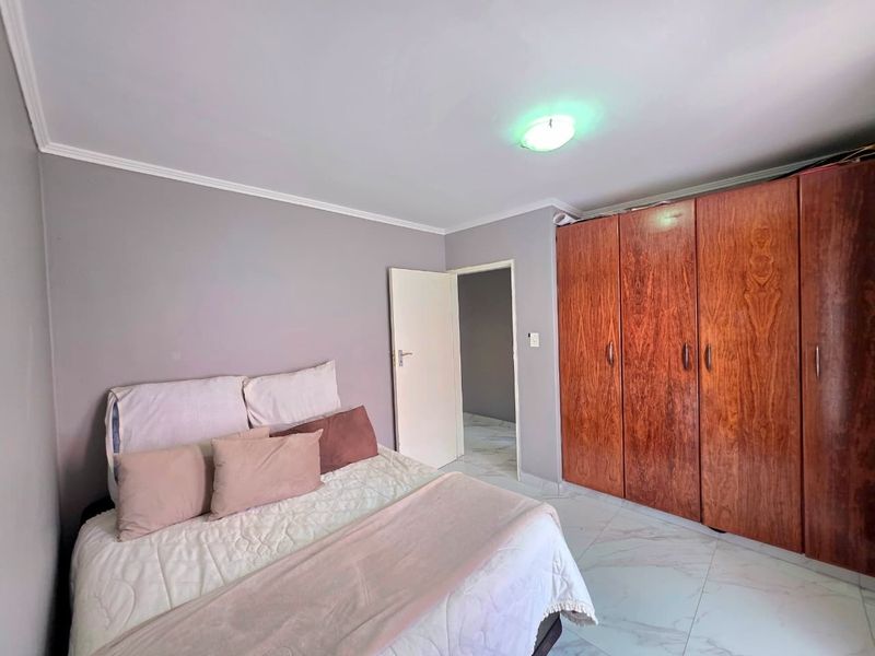 A bedroom featuring tiled flooring, coved ceilings, and a large built-in wooden wardrobe providing ample storage space.