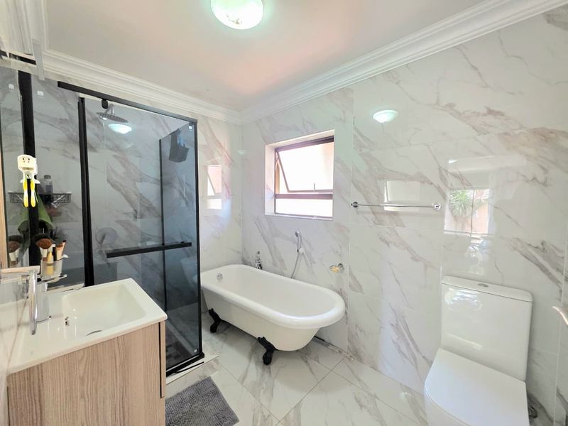 Modern bathroom featuring a freestanding bathtub, walk-in shower with black frame, vanity cabinet, and elegant marble-look wall and floor tiles.