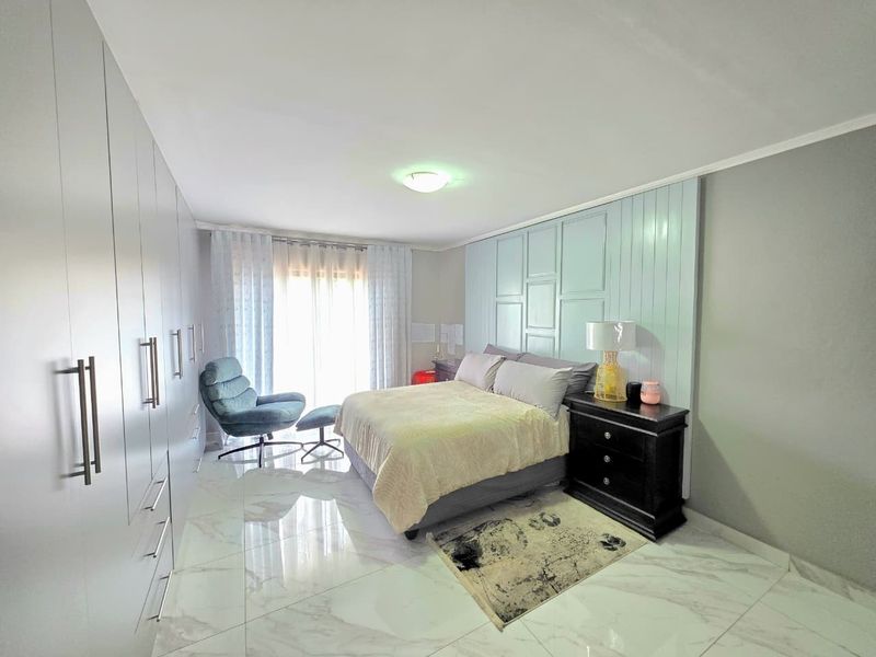 Spacious bedroom featuring modern tiled flooring, extensive built-in cupboards, and a decorative feature wall panel behind the bed area.