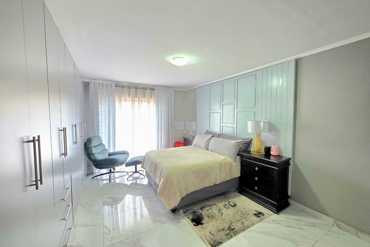 Spacious bedroom featuring modern tiled flooring, extensive built-in cupboards, and a decorative feature wall panel behind the bed area.