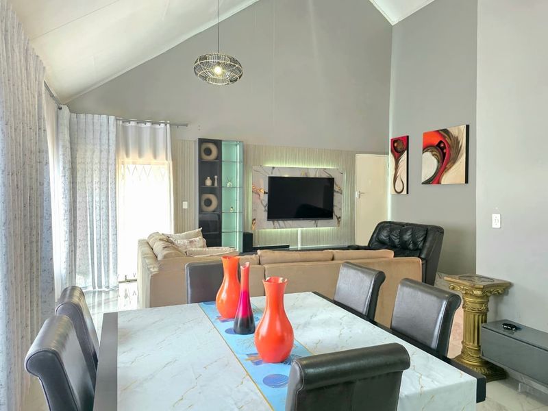 Spacious open-plan living and dining area featuring a dramatic vaulted ceiling, modern built-in media wall with marble accents, and integrated display shelving.