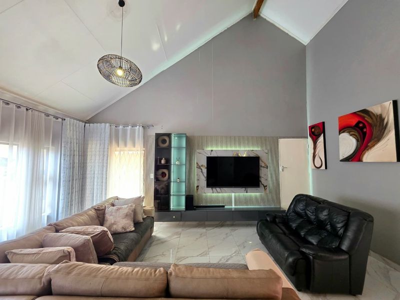 Spacious living room featuring a high vaulted ceiling, modern marble-look floor tiles, and a custom built-in media wall with integrated accent lighting.