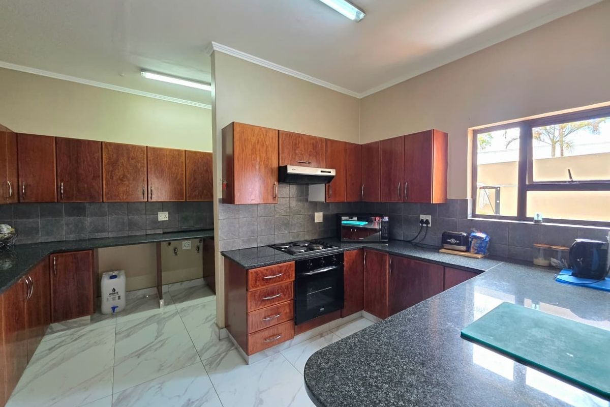 A functional kitchen featuring dark wood cabinetry, granite countertops, built-in oven with gas hob, and modern marble-look floor tiles.
