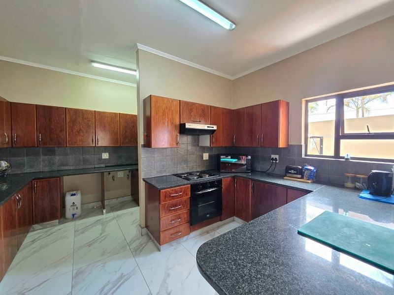 A functional kitchen featuring dark wood cabinetry, granite countertops, built-in oven with gas hob, and modern marble-look floor tiles.