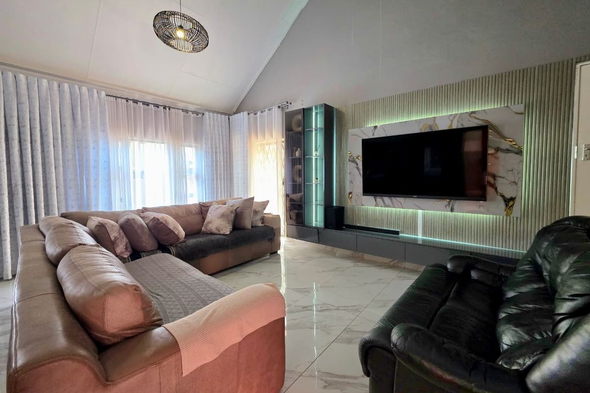 Modern living room featuring a high vaulted ceiling, polished marble-look floor tiles, and a sophisticated built-in media wall with integrated LED lighting.