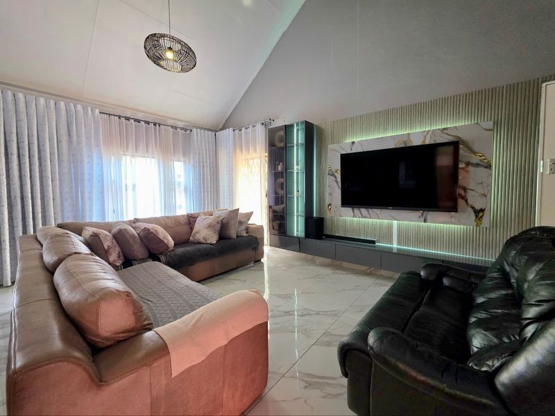Modern living room featuring a high vaulted ceiling, polished marble-look floor tiles, and a sophisticated built-in media wall with integrated LED lighting.