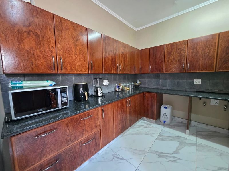 Functional kitchen featuring wood-look laminate cabinetry, granite countertops, dark tiled backsplash, and modern marble-effect floor tiles with dedicated appliance and plumbing connections.
