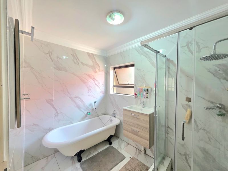 Modern bathroom featuring a freestanding bathtub, glass-enclosed rain shower, wall-mounted vanity, and elegant marble-look tiling throughout.