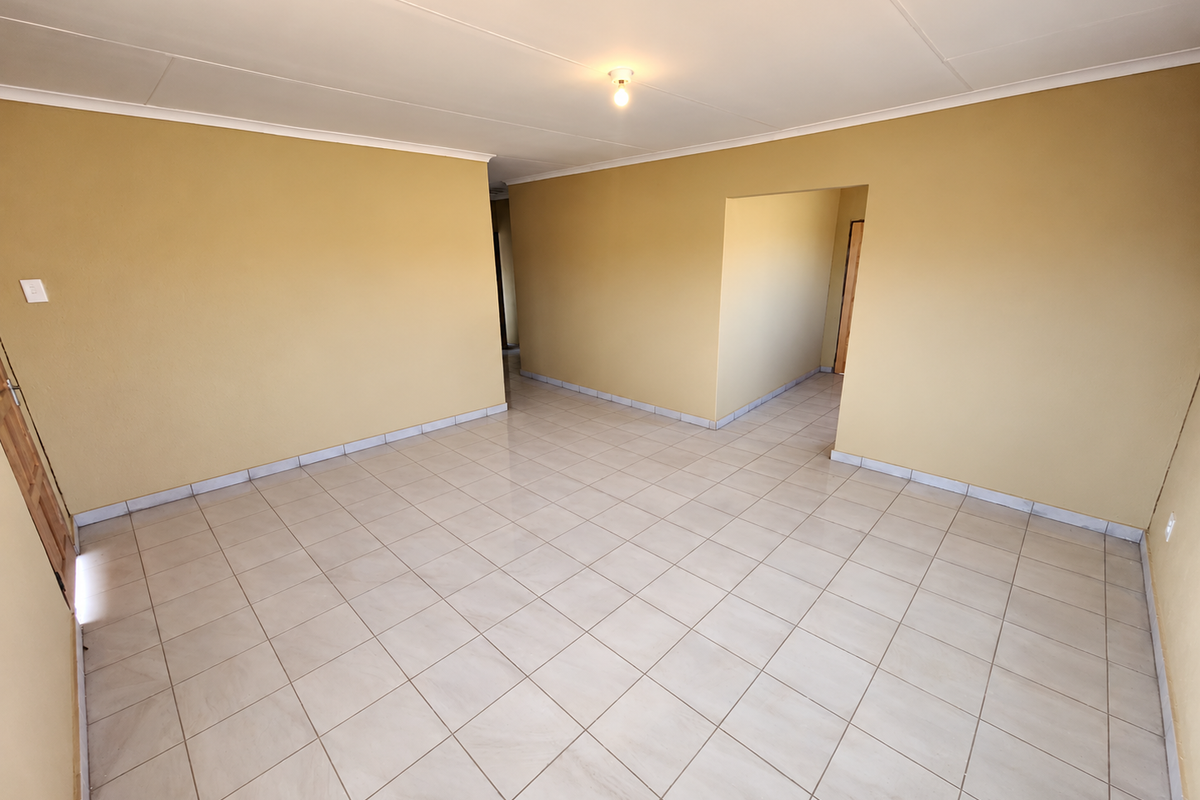 A spacious, empty living area featuring neutral tiled flooring and warm-toned walls, offering a versatile blank canvas for interior design.