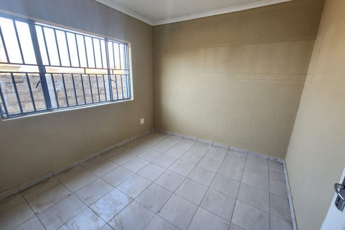 An empty bedroom featuring tiled flooring, neutral wall paint, and security bars on the window.