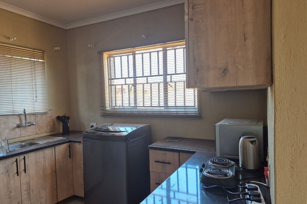 A functional kitchen featuring laminate cabinetry, granite countertops, and a built-in hob, with security bars installed on the windows.