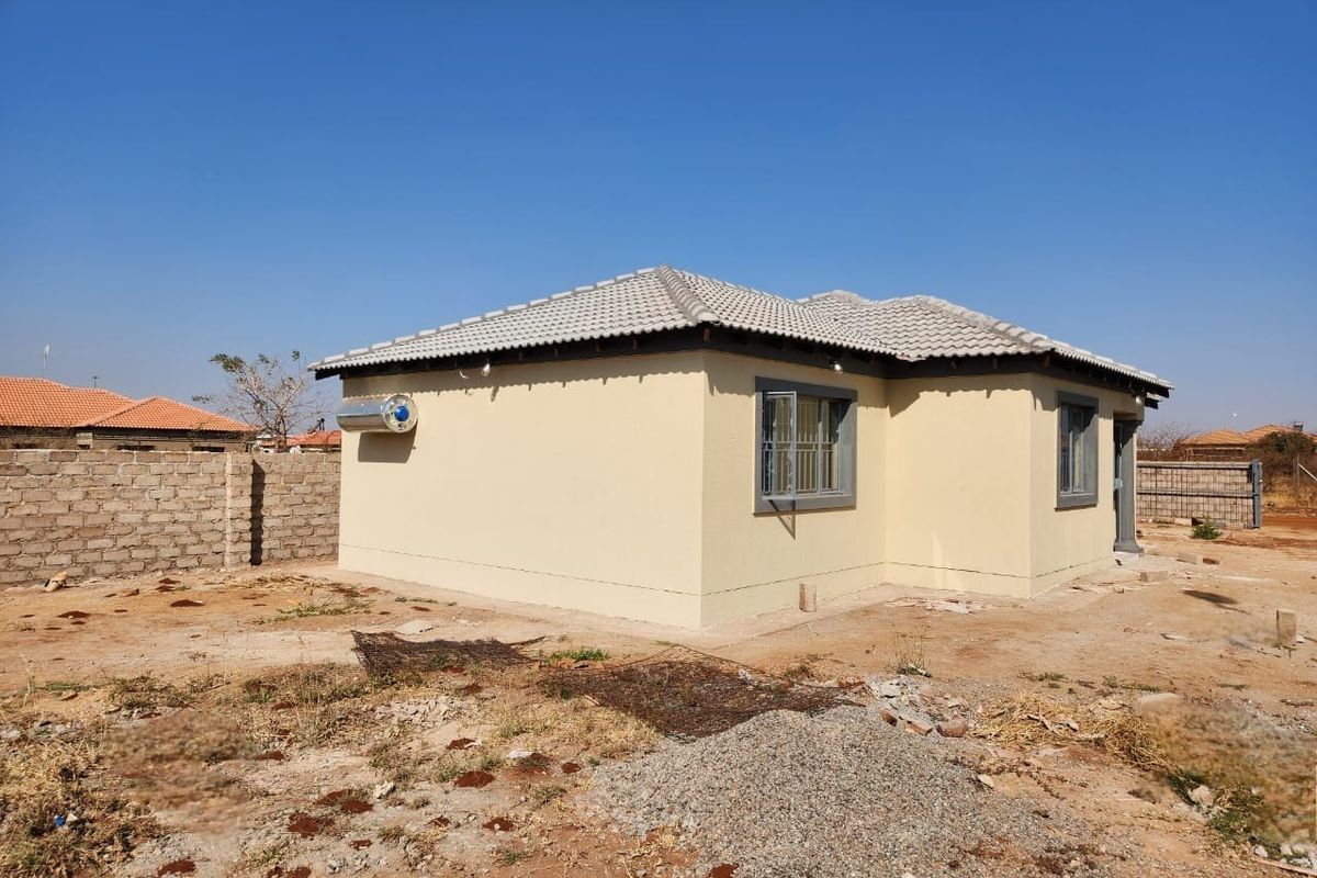 Rear view of a single-story house featuring a tiled roof, solar water heater, and security bars on windows, set on an unlandscaped plot.