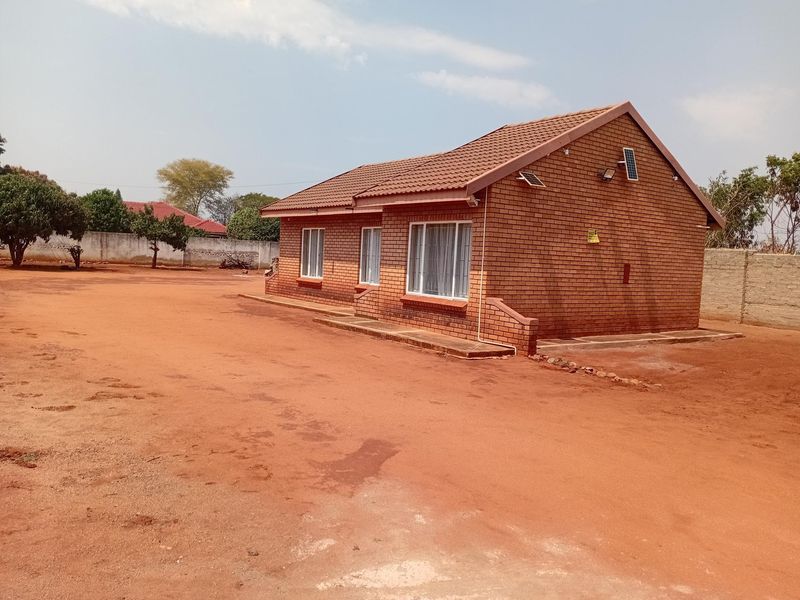 A view of the rear face brick house exterior featuring a tiled roof, aluminium windows, and a large unpaved yard area.