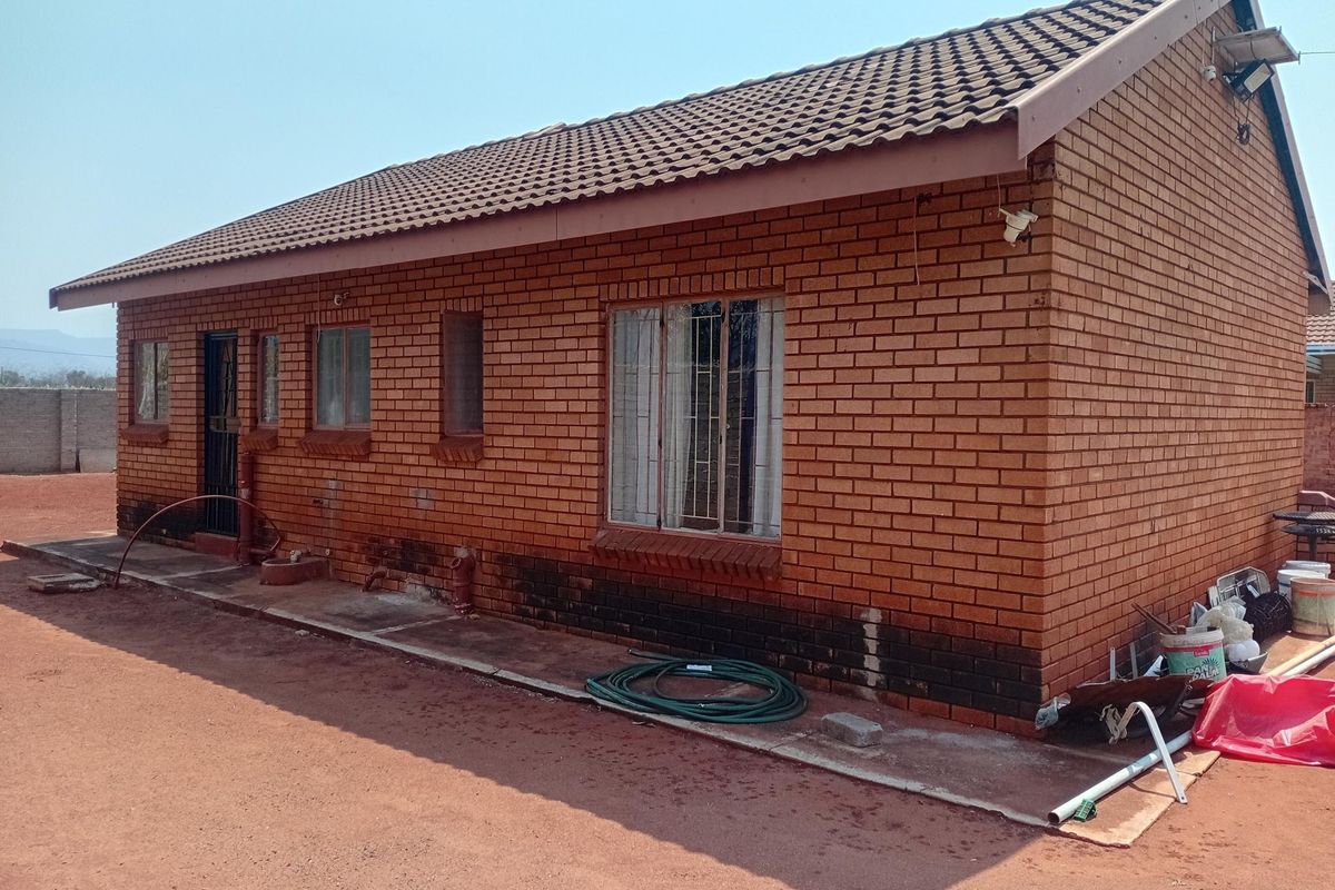 A side view of a face brick house featuring a tiled roof, security bars on windows, and a concrete apron surrounding the structure.