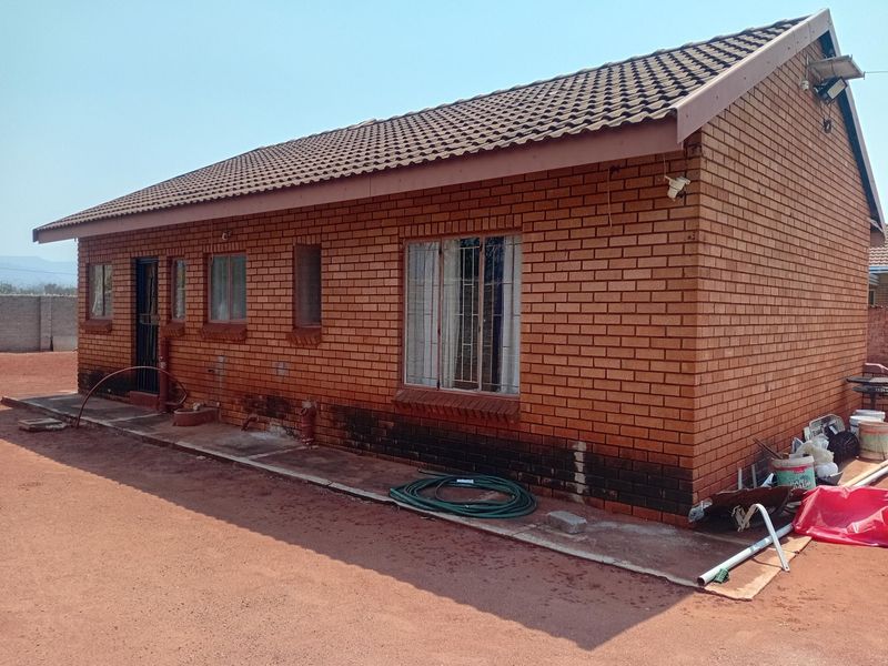 A side view of a face brick house featuring a tiled roof, security bars on windows, and a concrete apron surrounding the structure.