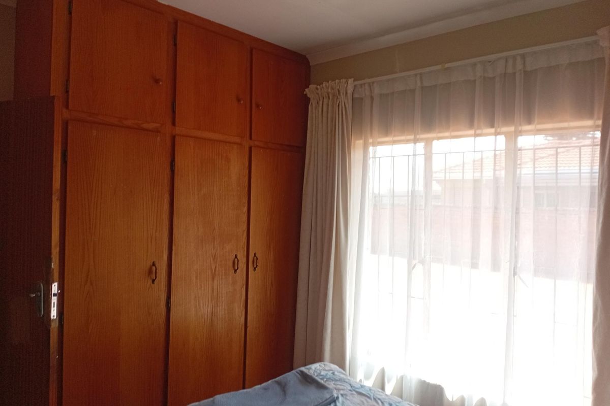 A bedroom featuring floor-to-ceiling built-in wooden cupboards and a window fitted with security bars, offering a functional and traditional layout.