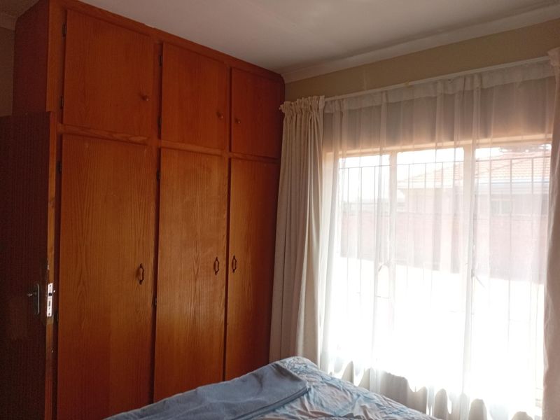 A bedroom featuring floor-to-ceiling built-in wooden cupboards and a window fitted with security bars, offering a functional and traditional layout.