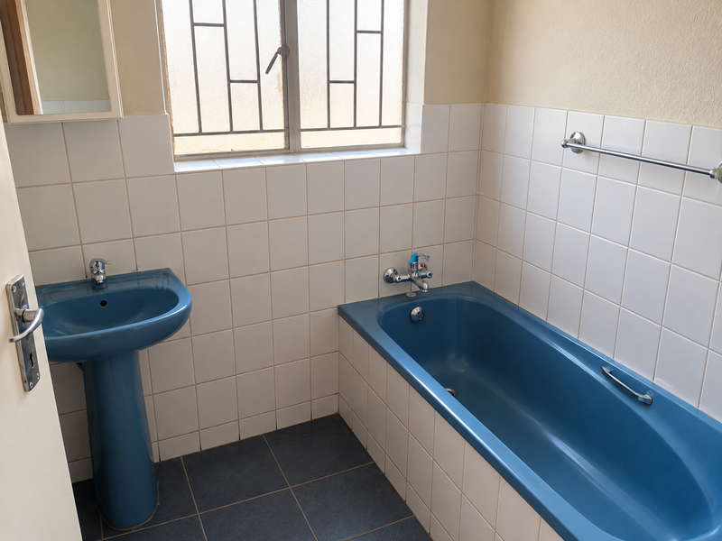 A functional bathroom featuring a blue pedestal basin and matching bathtub with white wall tiling and secure window bars.