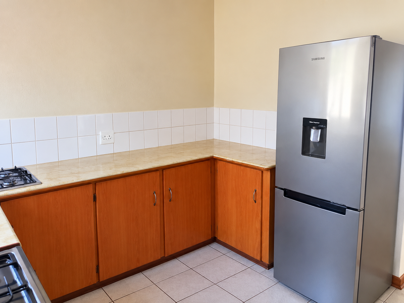A functional kitchen area featuring wooden cabinetry, laminate countertops, tiled splashback, and a built-in gas hob.