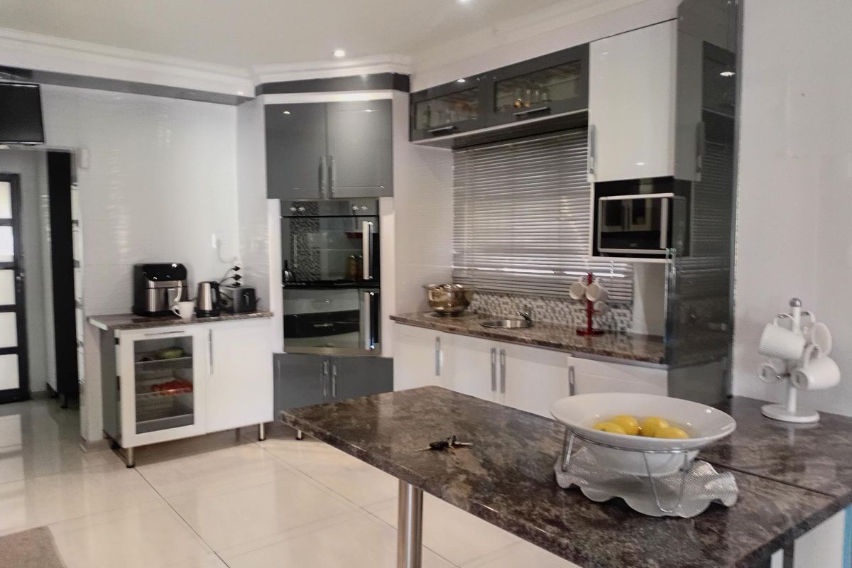 Modern kitchen featuring high-gloss cabinetry, granite countertops, built-in oven and microwave, and tiled flooring with recessed lighting.