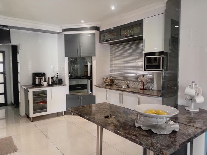 Modern kitchen featuring high-gloss cabinetry, granite countertops, built-in oven and microwave, and tiled flooring with recessed lighting.