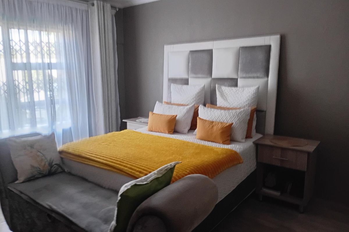 A well-maintained bedroom featuring laminate flooring, a large built-in headboard, and natural light through a window with security gate and curtains.
