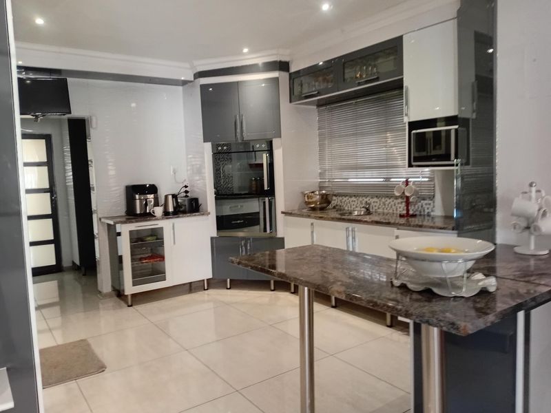 Modern kitchen featuring high-gloss cabinetry, granite countertops, integrated appliances, and tiled flooring with recessed lighting.