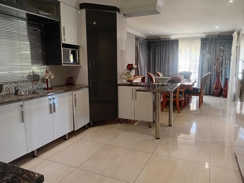 Modern open-plan kitchen and dining area featuring sleek cabinetry, granite countertops, a breakfast bar, and polished porcelain floor tiles.