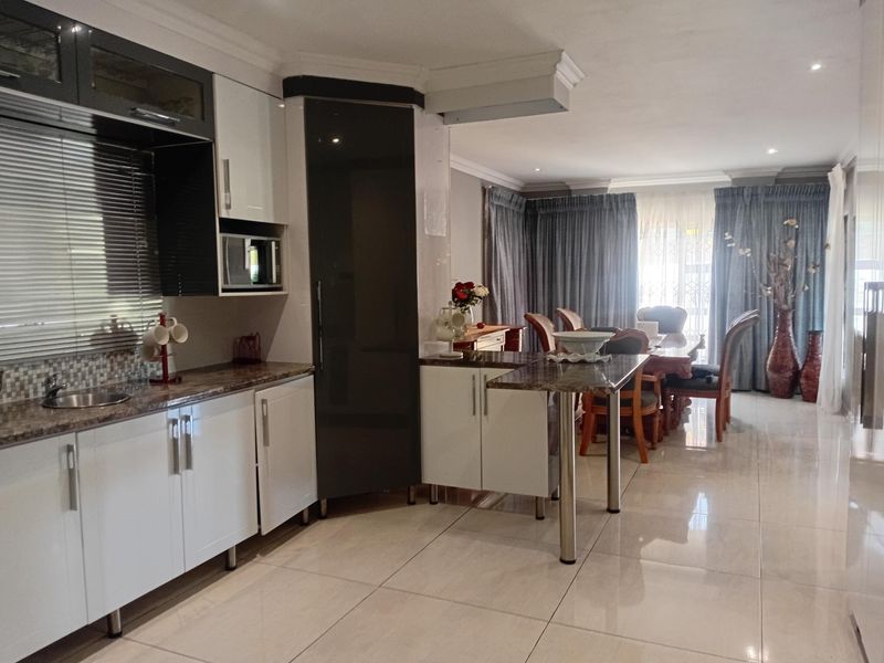 Modern open-plan kitchen and dining area featuring sleek cabinetry, granite countertops, built-in microwave, and polished tiled flooring throughout.