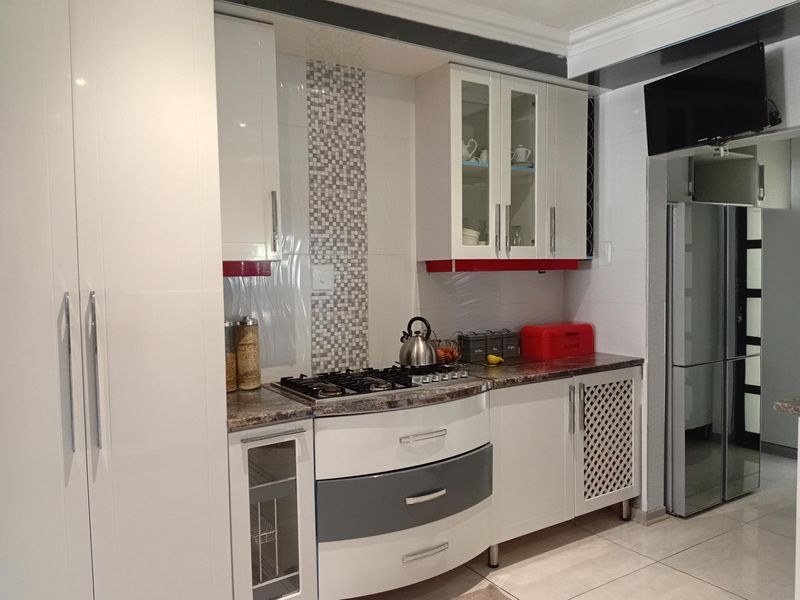 A modern kitchen featuring white and grey cabinetry, a gas hob, stone countertops, and a decorative mosaic tile backsplash.