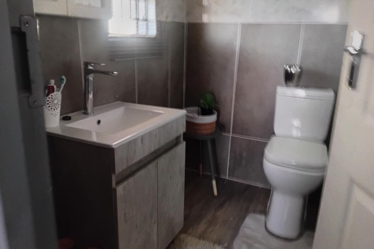 A compact bathroom featuring a modern vanity with basin, mixer tap, and a standard toilet, finished with neutral wall tiling.